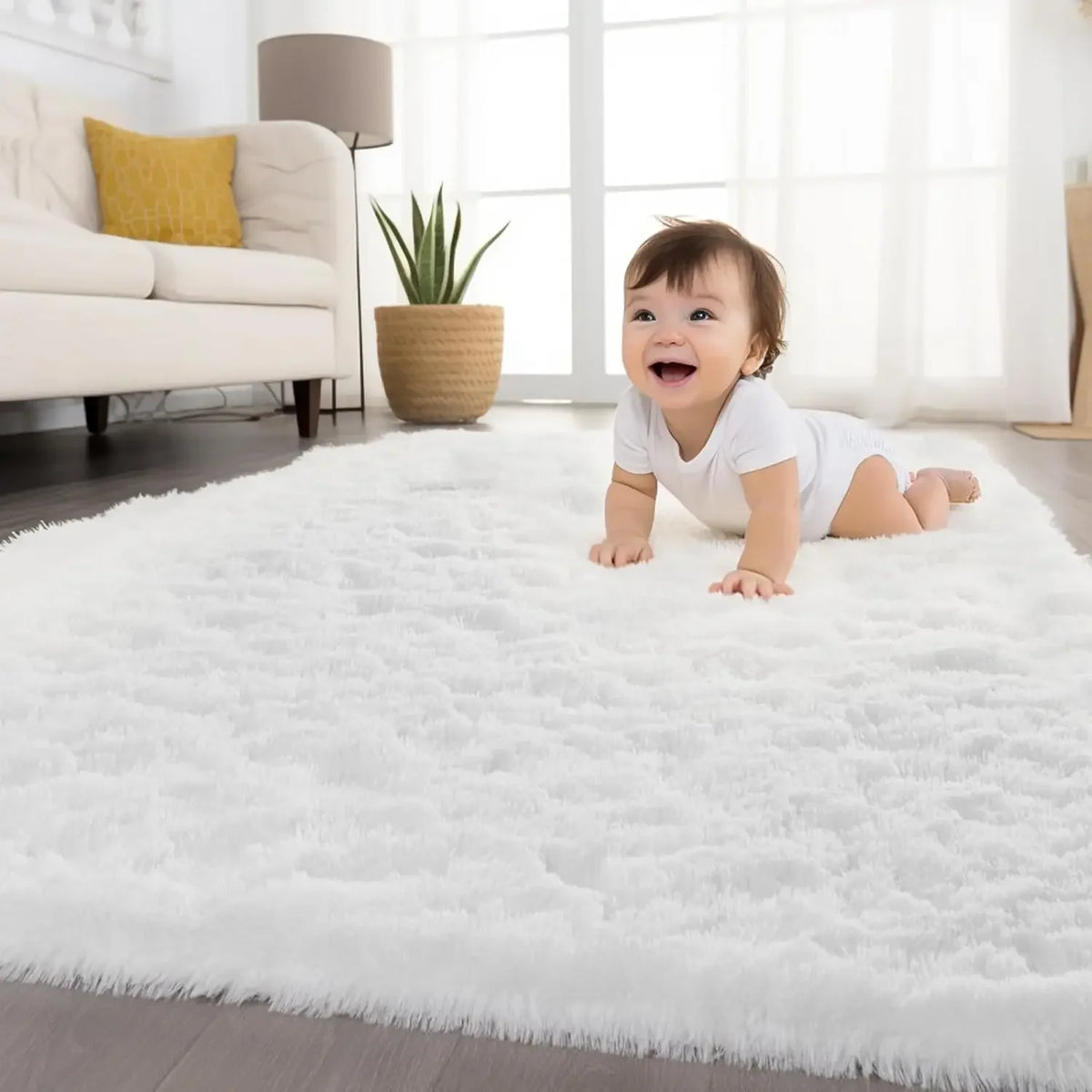 A baby lying on a fluffy white carpet in a bright room with a sofa and potted plant visible.