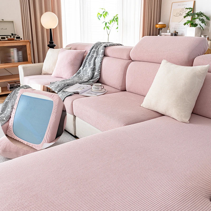 A pink plush elastic sofa cushion cover with light pink upholstery and decorative pillows.