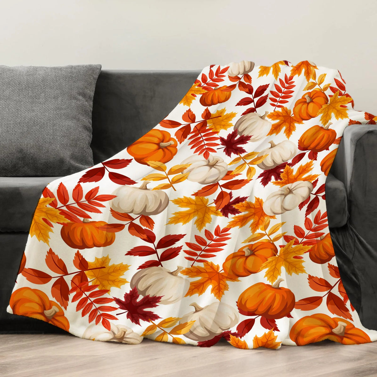 An orange and green maple leaf pattern flannel throw blanket draped over a gray sofa.