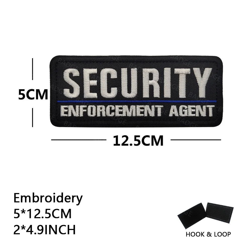 Black embroidered security enforcement agent patch measuring 5cm by 12.5cm with a hook and loop.