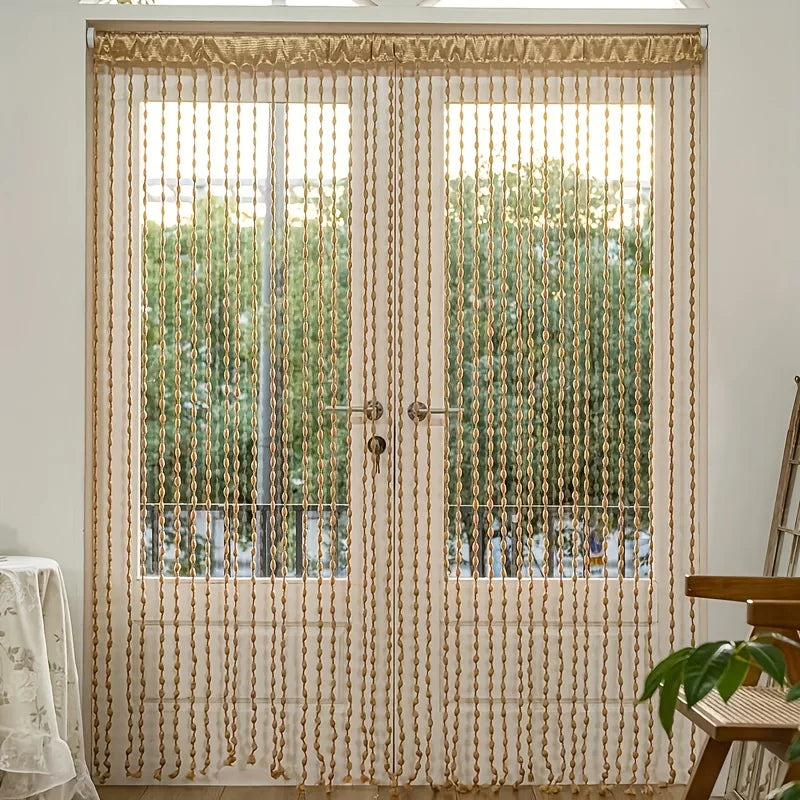 A pair of sheer fabric door curtains with long gold tassels covering a window.