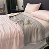 A pink and gray reversible cooling quilt is displayed on a bed with soft pillows.