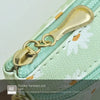Gold hardware pull on a light green PU leather coin purse with a textured fabric background