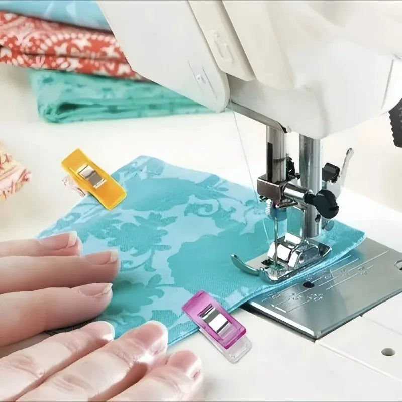 Hands are placing a yellow clip onto a blue fabric under a sewing machine.