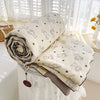 A rolled white quilt with a floral pattern is displayed on a white table covered with a sheer white cloth.