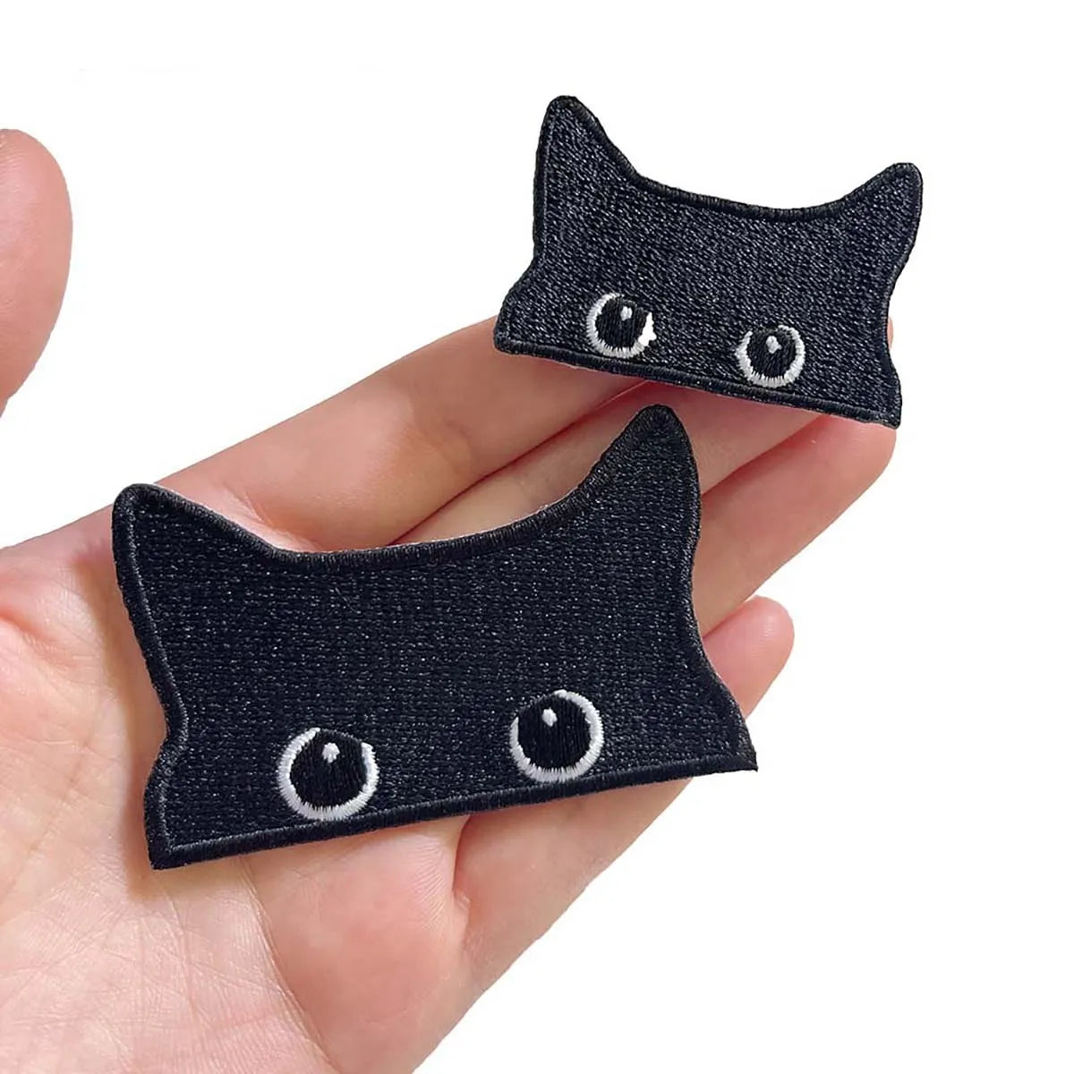 A pair of embroidered black cat iron-on patches are shown being held in a hand.