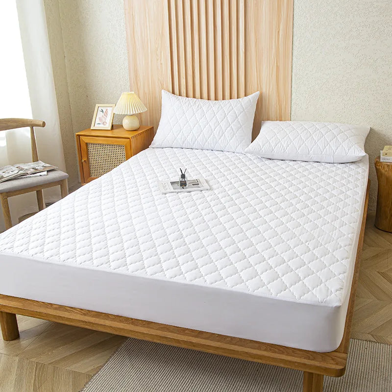 A white waterproof mattress protector fitted sheet is displayed on a wooden bed frame with a light-colored headboard.