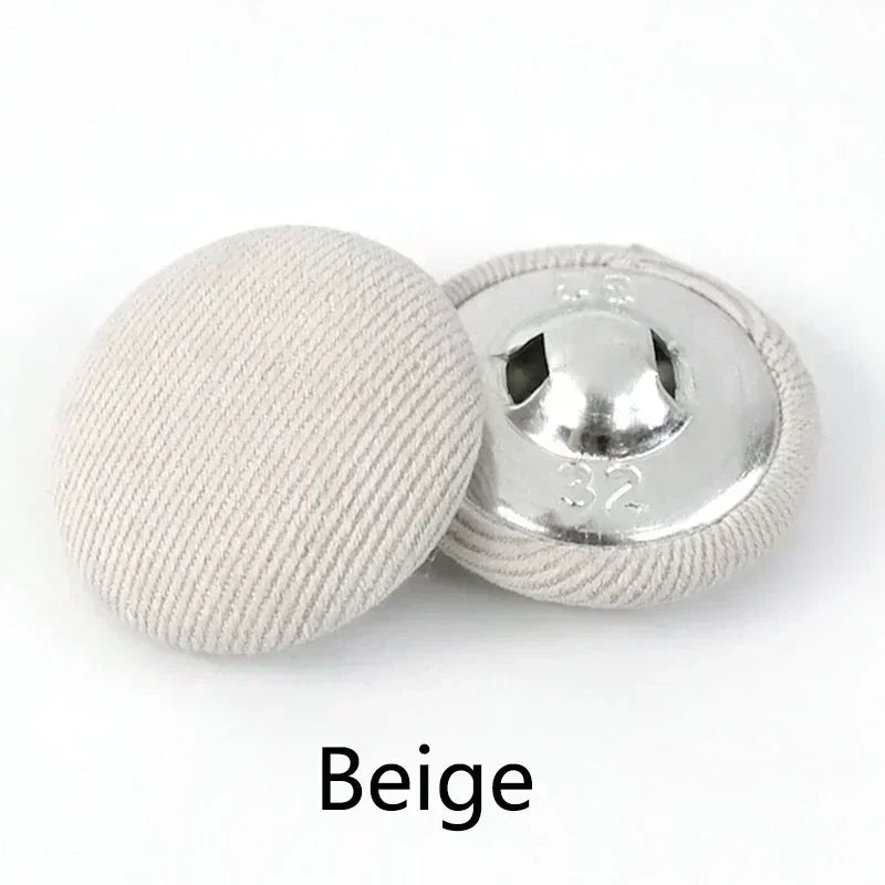 A beige round fabric-covered shank button is shown next to its silver metal base.