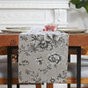 A gray floral patterned checkered table runner displayed on a wooden dining table.
