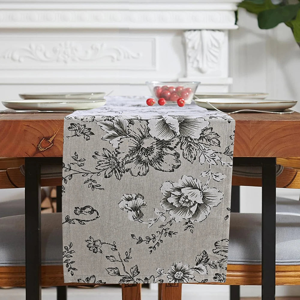 A gray floral patterned checkered table runner displayed on a wooden dining table.