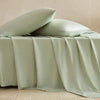 A light sage green bamboo fiber flat bed sheet draped over a bed, with two pillows resting on top.