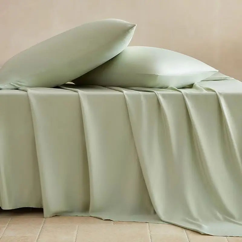 A light sage green bamboo fiber flat bed sheet draped over a bed, with two pillows resting on top.