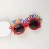 Red birthday candle hat shaped like sunglasses with the words HAPPY BIRTHDAY spelled out in colorful letters