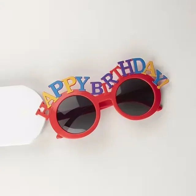 Red birthday candle hat shaped like sunglasses with the words HAPPY BIRTHDAY spelled out in colorful letters