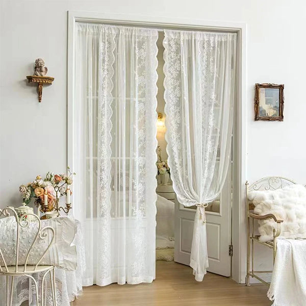 White sheer floral lace window curtains hanging in a light-colored room.