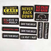 A collection of black embroidered alphabet hook and loop patches with motivational phrases in yellow, red, and white.