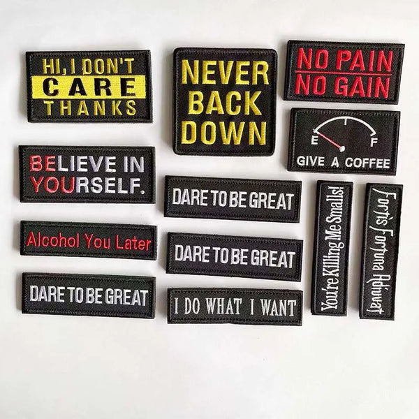 A collection of black embroidered alphabet hook and loop patches with motivational phrases in yellow, red, and white.