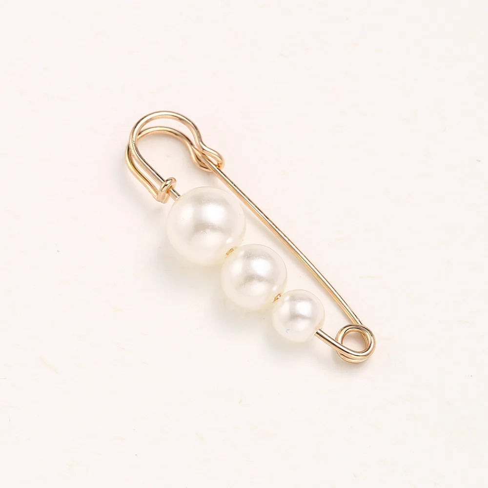 Gold-toned adjustable pearl brooch featuring a chain and three round pearls.