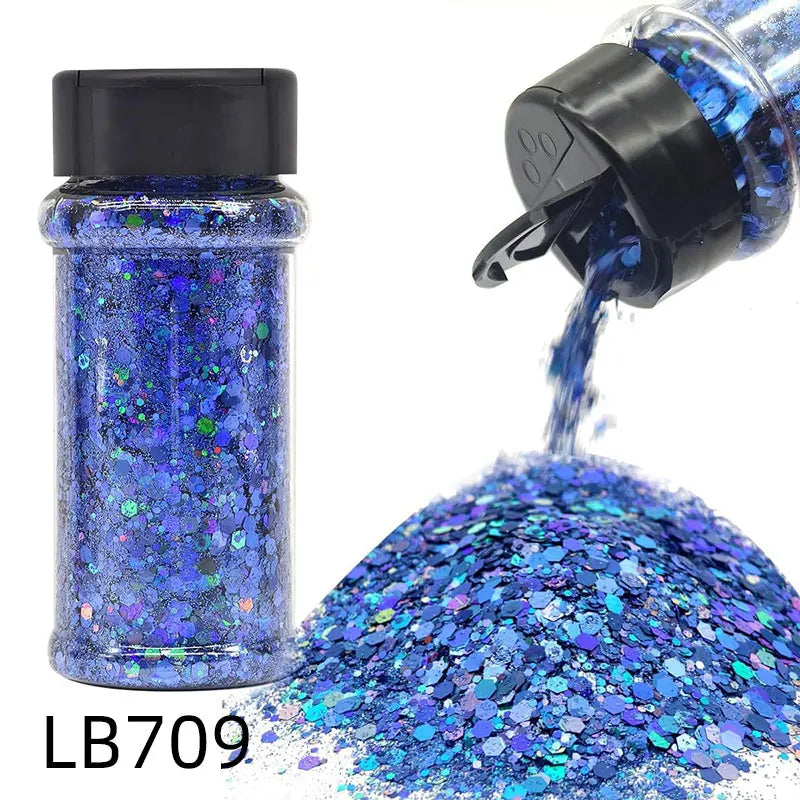 A glass bottle of blue holographic glitter mix with a black cap and a pile of loose glitter.