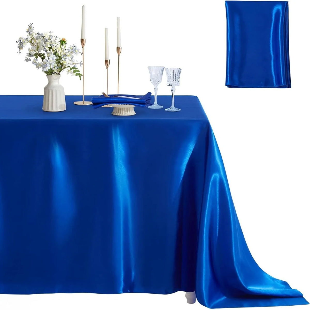A royal blue satin tablecloth set for elegant dining featuring a centerpiece of white flowers, candles, and glassware.