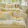 A bed with a duvet and pillow set featuring yellow, cream, and sage green geometric patterns.