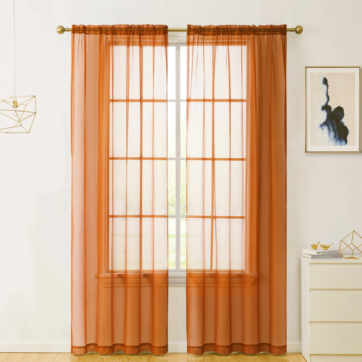 A pair of sheer orange voile curtains hanging on a window with a light-colored trim.