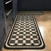 A rectangular floor mat with a black and beige geometric pattern placed on a light wood floor.