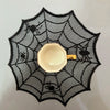 A black mesh table runner placemat featuring a spider design and a small white cup.