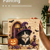 A person holds a finished diamond painting featuring a purple cat and an orange pumpkin on a framed canvas.