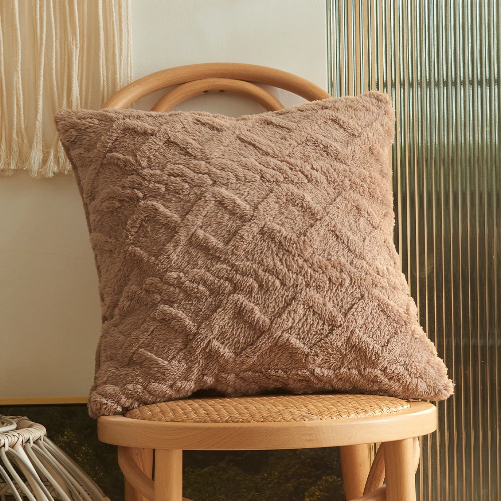 A textured taupe plaid cushion cover resting on a light wood stool against a vertical ribbed background.