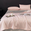 A soft pink lightweight cooling blanket is displayed on a bed with matching pillows and a candle.