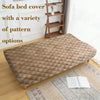 A beige quilted sofa bed cover with a variety of pattern options displayed on a wooden shelf.