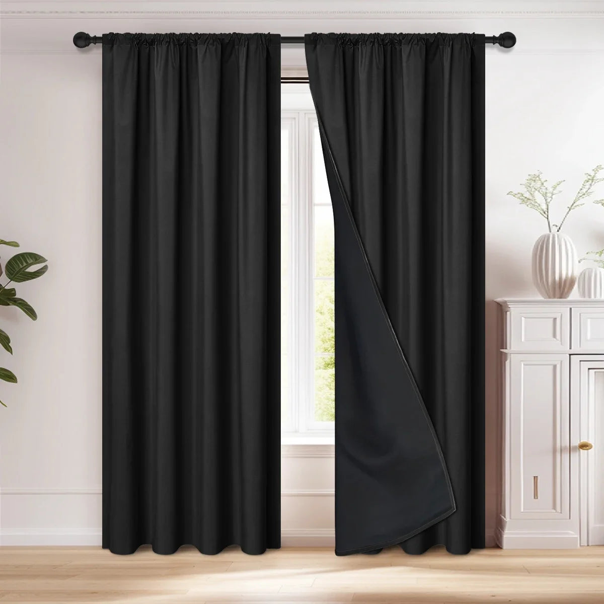 A pair of black blackout curtains hanging on a rod, shown next to a window.