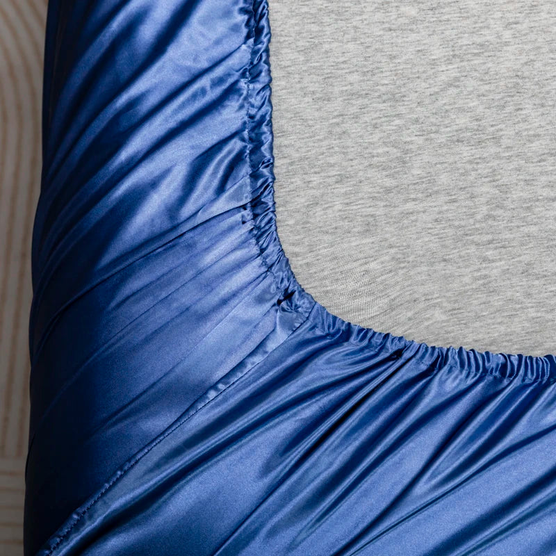 Close-up of a royal blue satin fitted sheet with gathered elastic at the waistband.