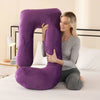 A woman is hugging a purple J-shaped ergonomic maternity pillow on a white bed.