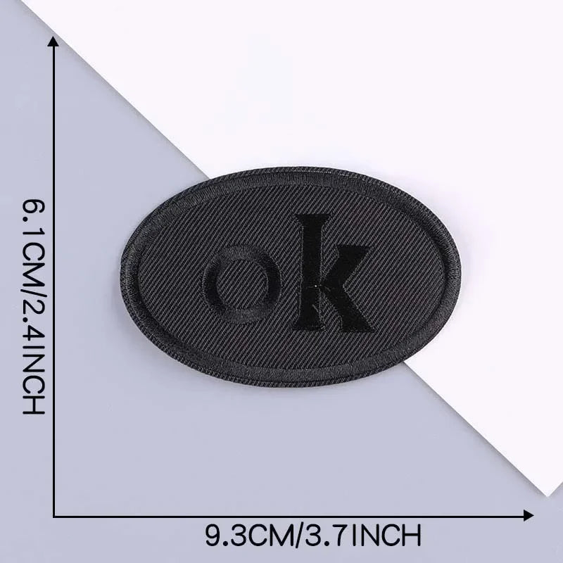 A black embroidered leather patch with the letter OK on it, shown against a white background.
