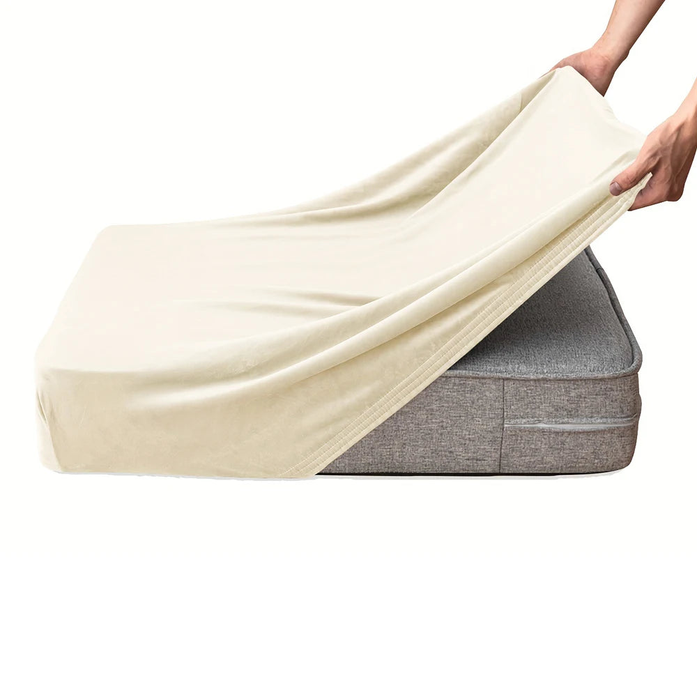 A hand is draping a cream-colored velvet stretchy sofa seat cover over a gray sofa cushion.