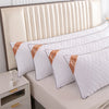 A set of white rectangular sleeping pillows with gold trim resting against a light-colored headboard.