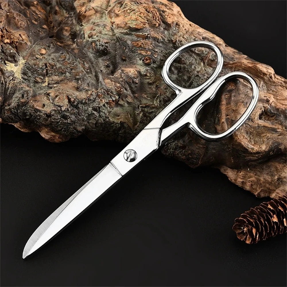 A pair of professional stainless steel sewing scissors resting on a rough piece of wood.