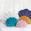 A collection of velvet stuffed sofa cushions shaped like decorative seashells in shades of purple, white, yellow, and teal.