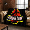 A black flannel throw blanket featuring a red dinosaur silhouette and the text Jurassic Park in yellow and white.