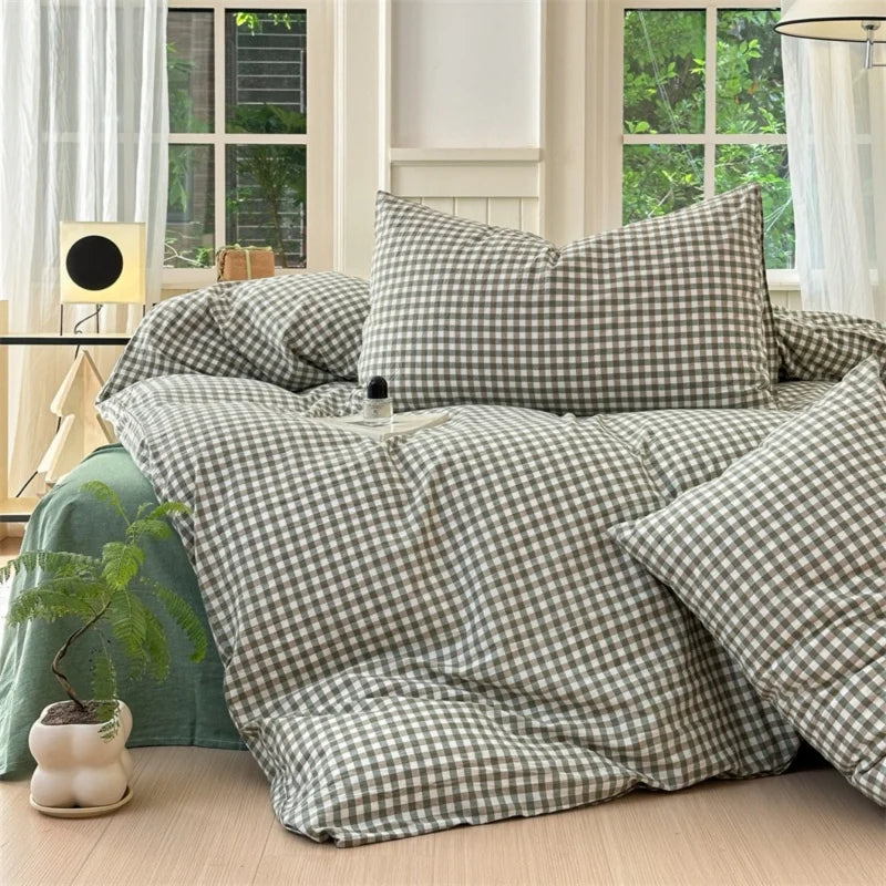 A set of three plaid duvet covers and pillowcases in olive green and beige tones displayed on a bed.