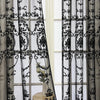 Black sheer curtain featuring intricate lace embroidery and pearl detailing hanging in a window.