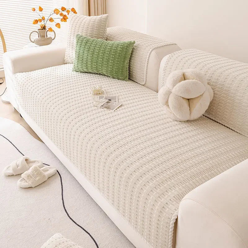 A white sofa cover with a textured knit fabric and decorative pillows in shades of green and cream.