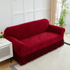 A deep red anti-slip jacquard sofa slipcover placed on a light rug in a bright room.
