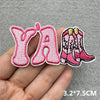 Pink embroidered patches spelling out YA and a pair of pink boots on a hand