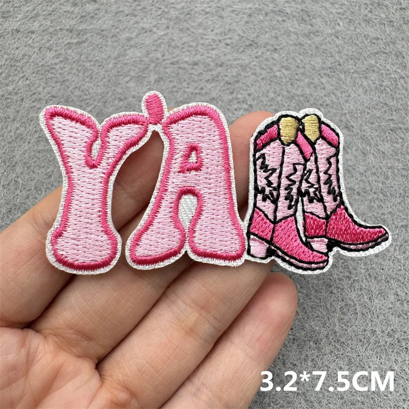 Pink embroidered patches spelling out YA and a pair of pink boots on a hand