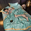 A teal luxury ice silk summer blanket set is draped on a bed, with a person lying under the fabric.