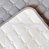 A white quilted mattress protector with a gray quilted cover visible.