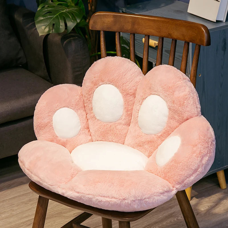 A pink plush bear paw cushion resting on a wooden chair.